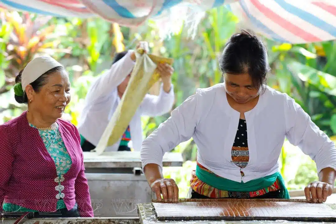 A papermaker working over a trough, with finished sheets stacked behind